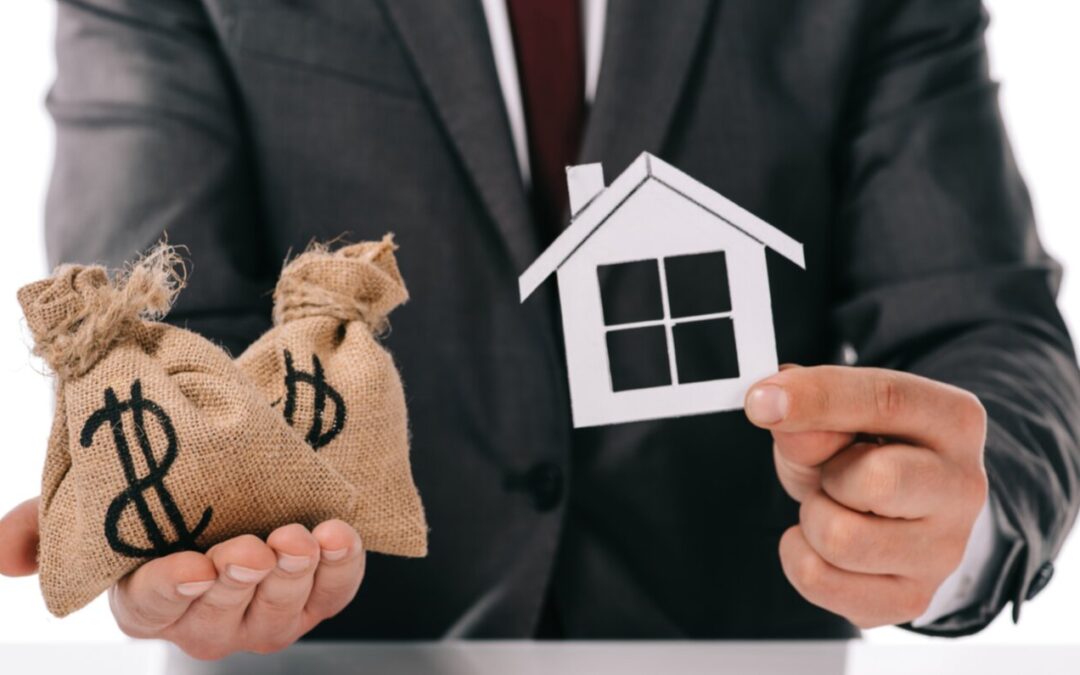 Homme qui tient une petite maison en papier dans une main et deux sacs d'argent dans l'autre