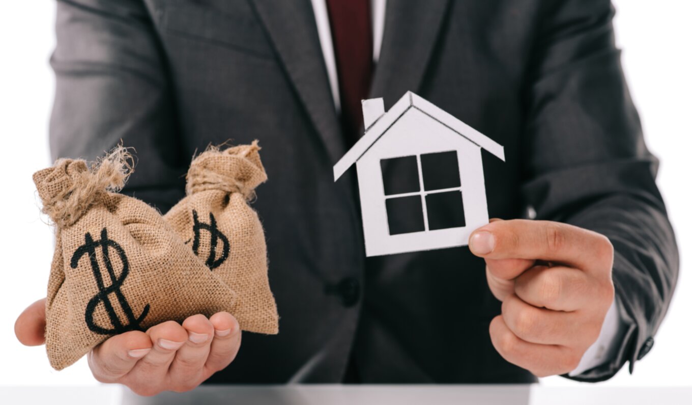 Homme qui tient une petite maison en papier dans une main et deux sacs d'argent dans l'autre