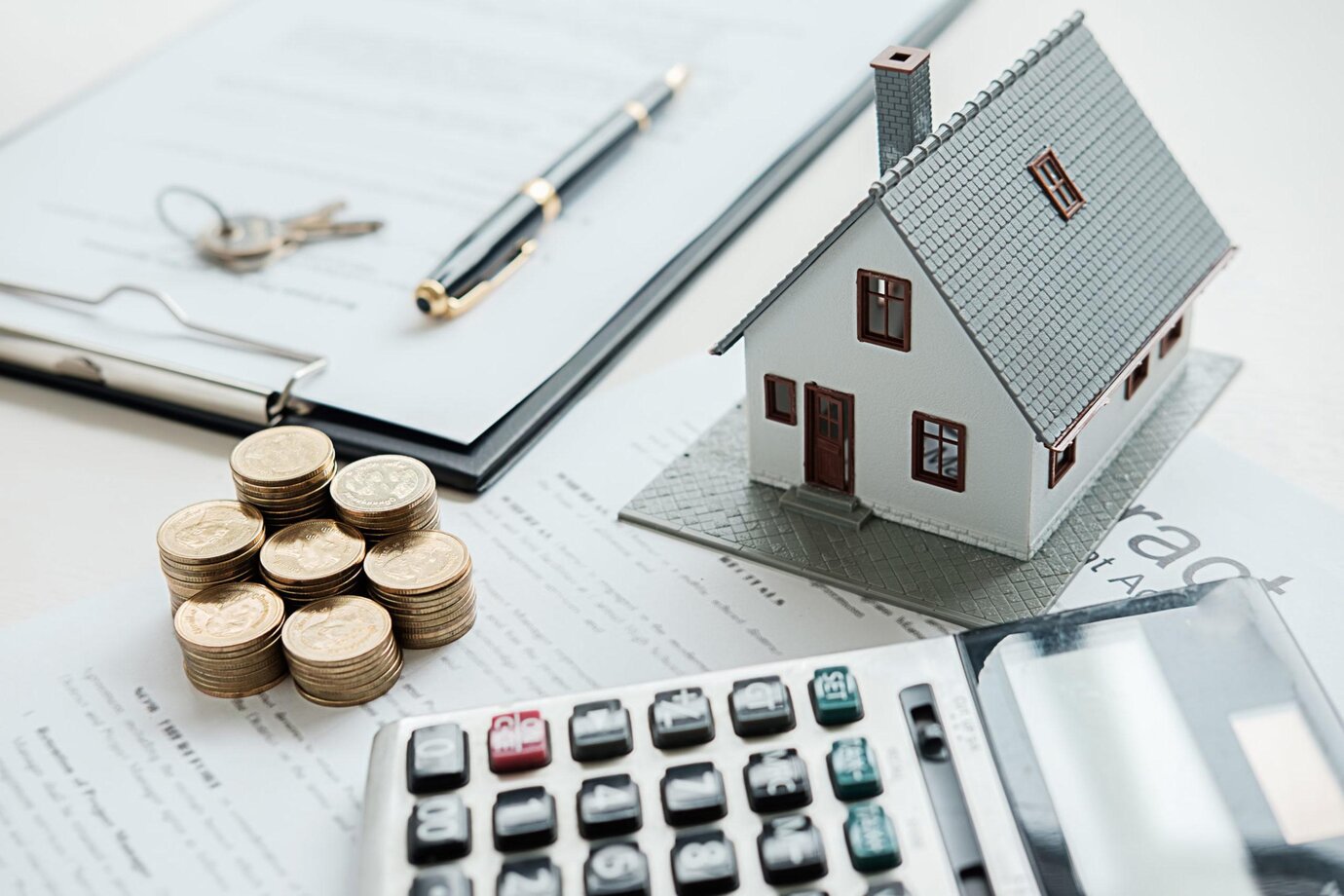 Maison miniature avec calculatrice et pile de pièce sur un contrat avec un stylo