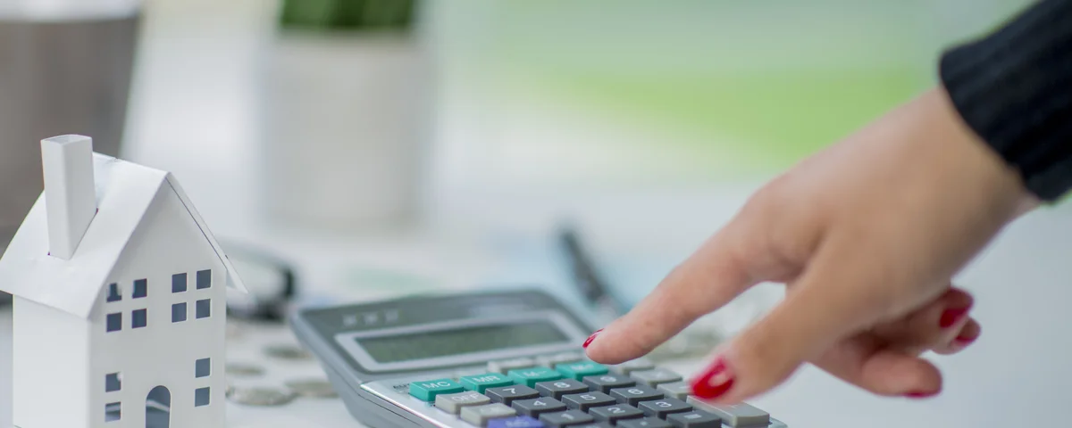 Main de femme tapant sur une calculatrice posée à côté d'une maison miniature